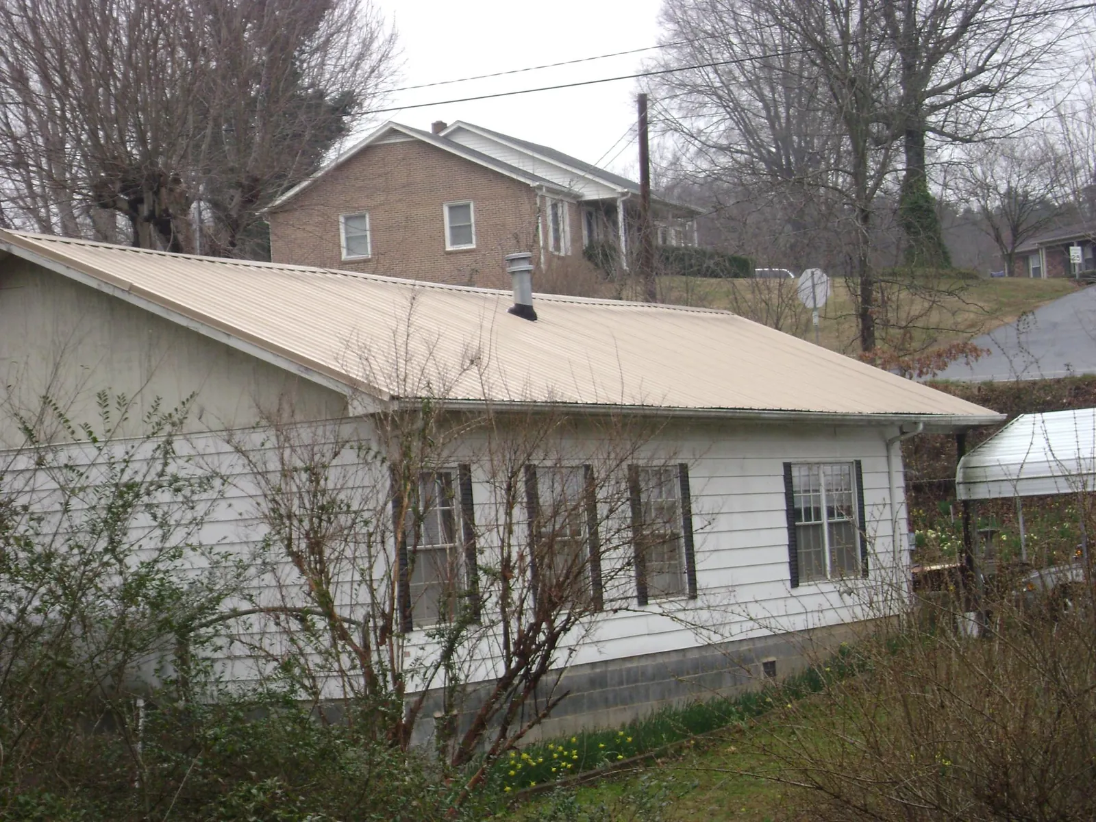 Tan metal roof on a white sided house set into a hillside — Commercial Roofing by Roofing Brothers in Bridgeport